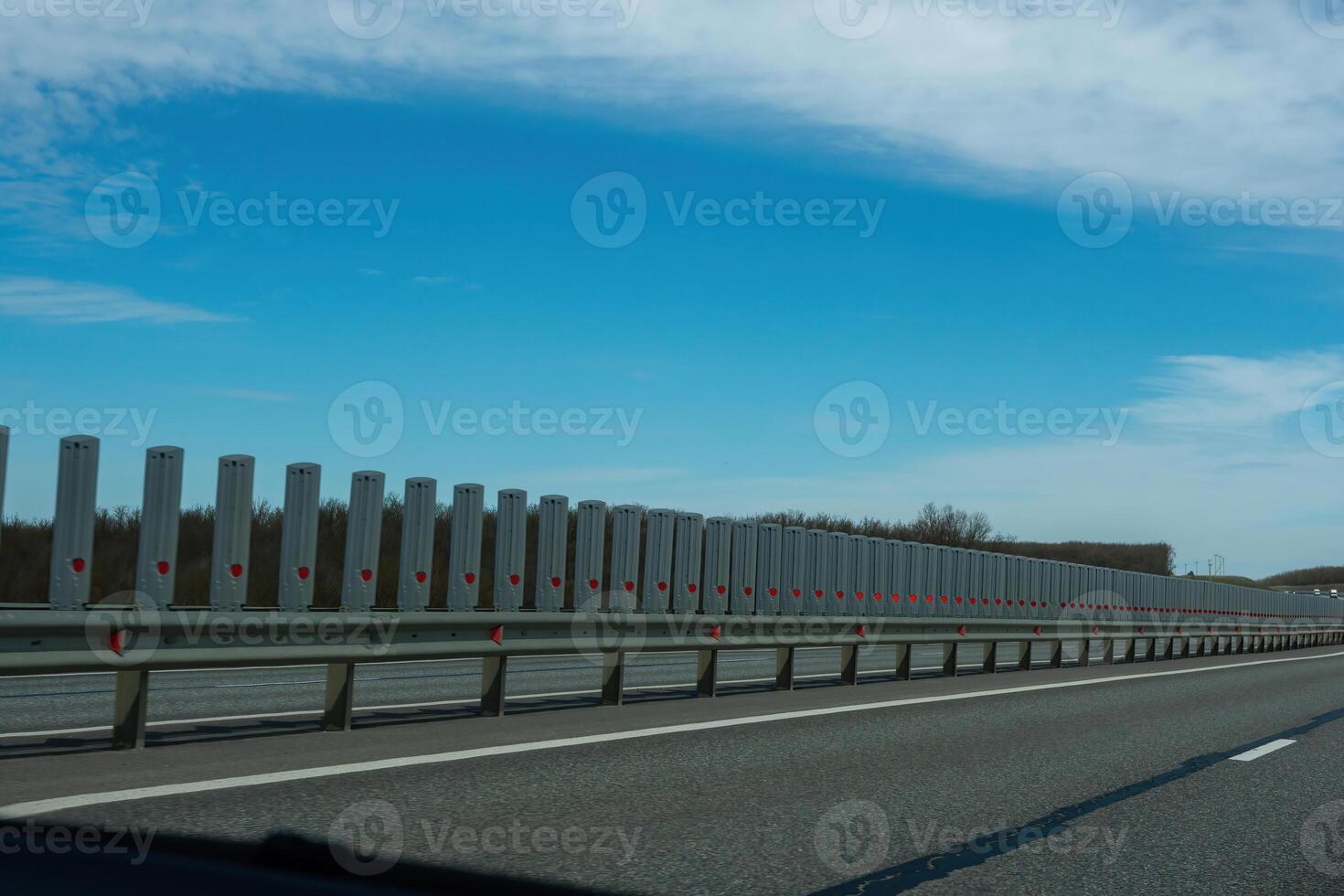 A road with a long line of metal posts with red hearts on them. The road is empty and the sky is clear. photo