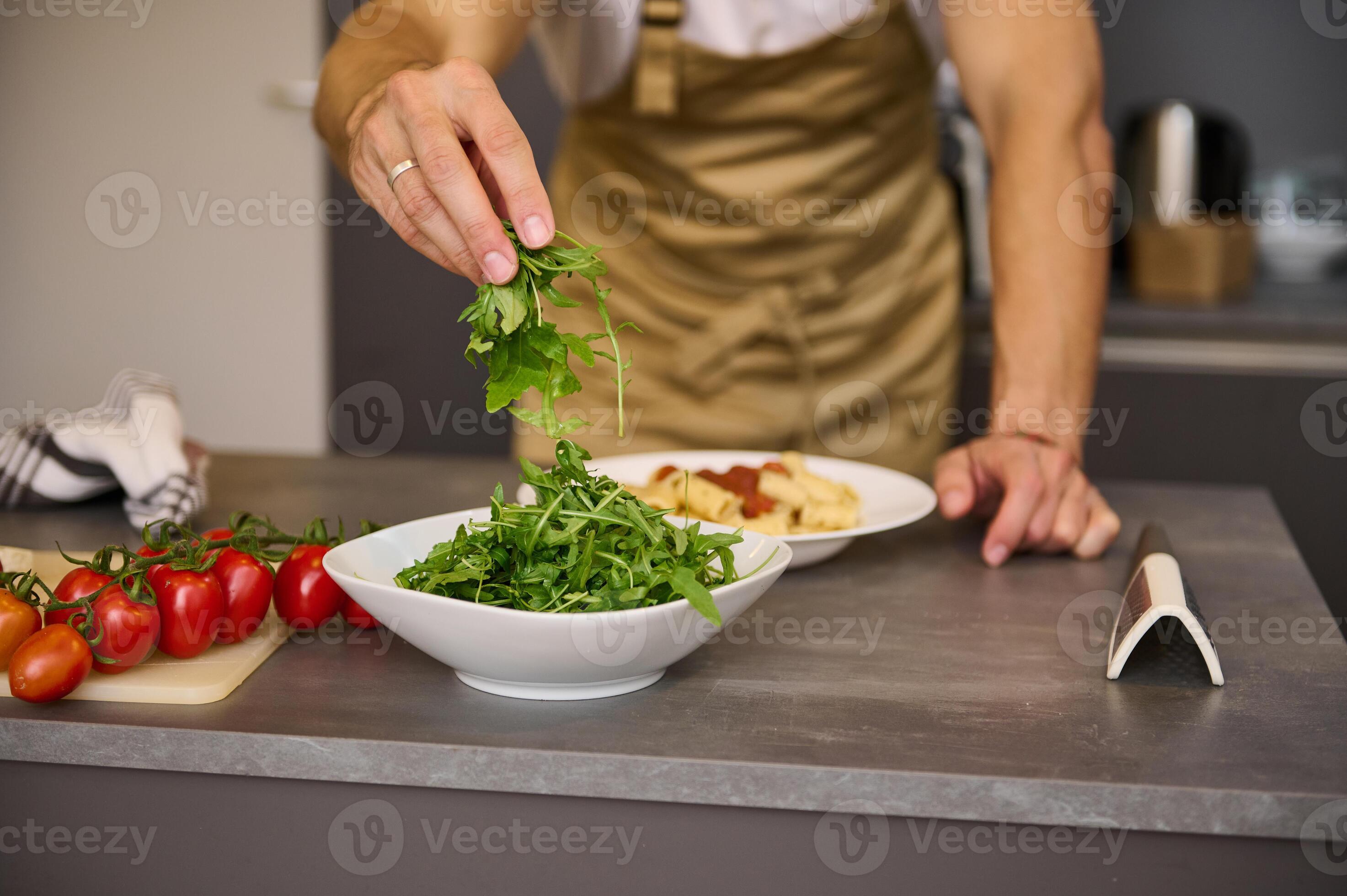Closeup chef hands holding fresh arugula leaves, garnishing meal, cooking Italian spaghetti in