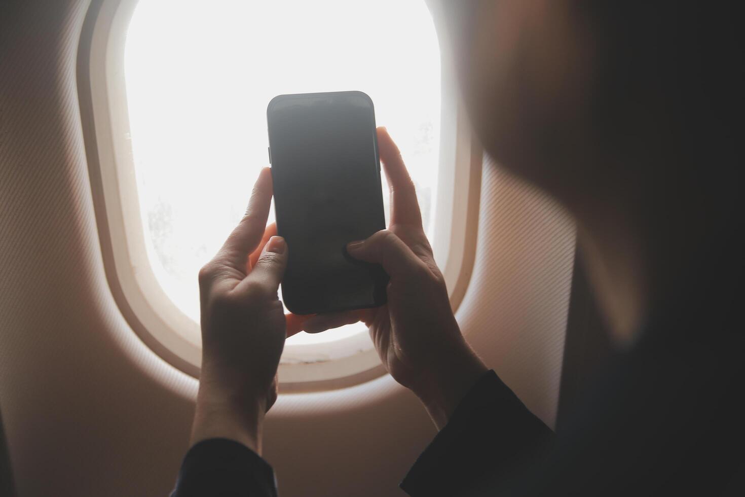 Blonde female tourist checking incoming notification on smartphone sitting on seat of airplane with netbook.Young businesswoman share media from telephone on laptop computer during plane flight photo