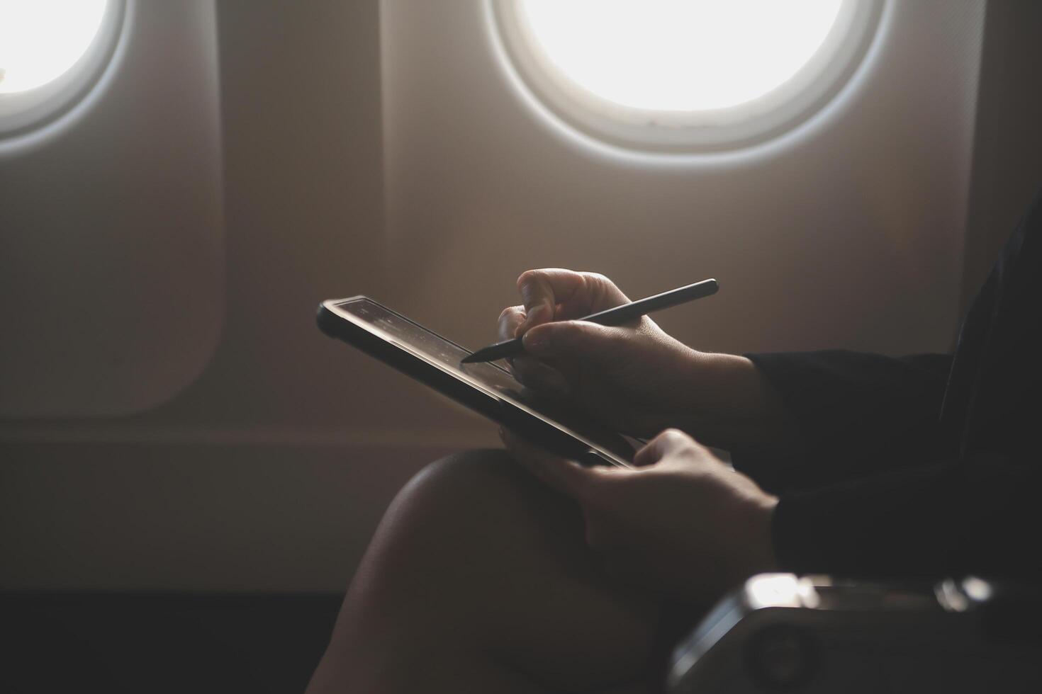 Blonde female tourist checking incoming notification on smartphone sitting on seat of airplane with netbook.Young businesswoman share media from telephone on laptop computer during plane flight photo