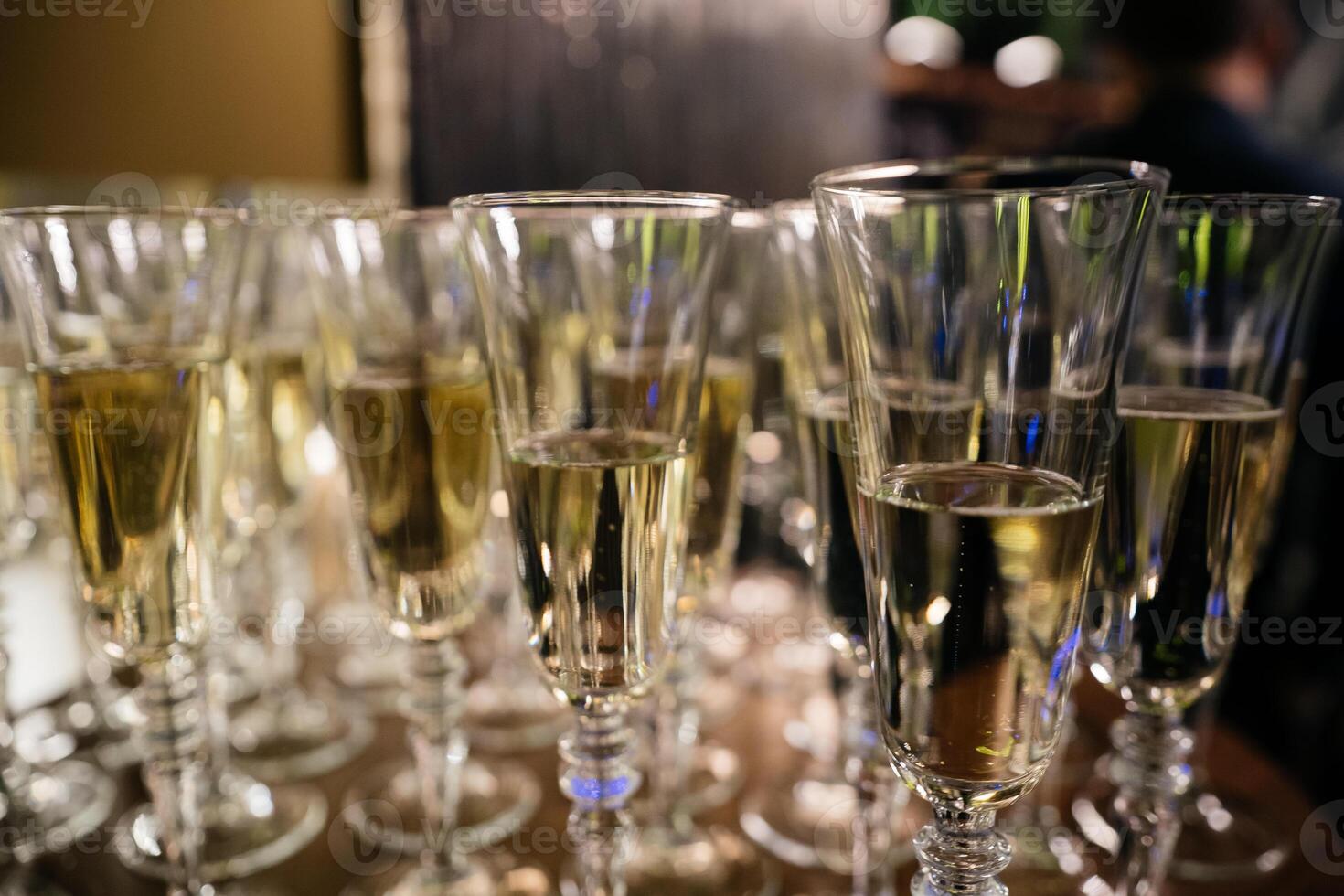 A row of wine glasses are lined up on a table. The glasses are all filled with a clear liquid, and they are all the same size. photo