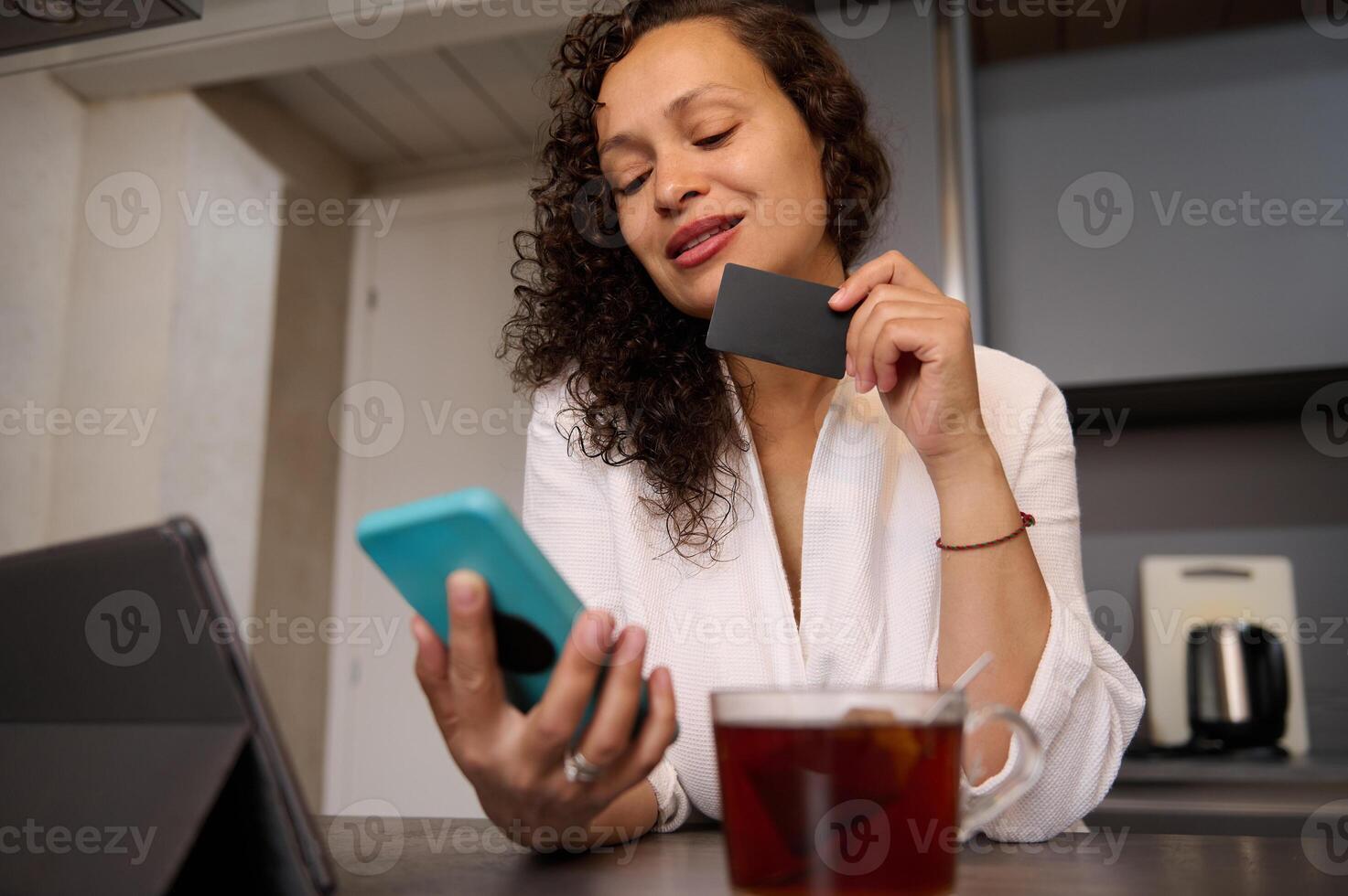 Smiling woman at home kitchen, using mobile phone and online shopping, paying bills online via internet mobile banking application photo