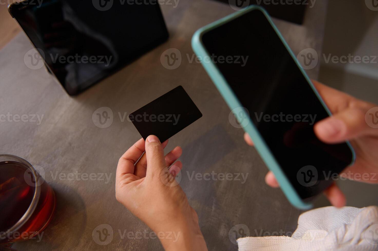 Close-up female hands hold a black mockup credit card with copy ad space for text, and using smart phone for online shopping, receiving or making payments via internet mobile banking application photo