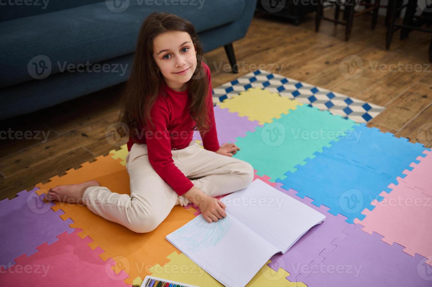 Adorable little school girl at home, doing homework, writing on copy book, smiling looking at camera photo