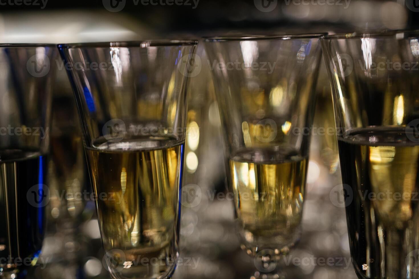 A row of wine glasses are lined up on a table. The glasses are all filled with a clear liquid, and they are all the same size. photo