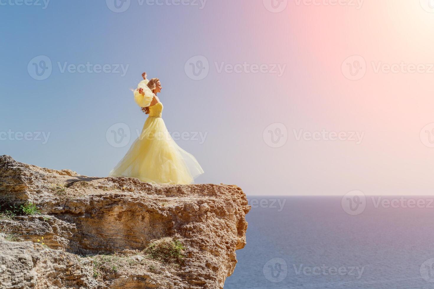 mujer en un amarillo vestir en el mar. lado ver joven hermosa sensual mujer en amarillo largo vestir posando en un rock alto encima el mar a puesta de sol. niña en naturaleza en contra el azul cielo foto