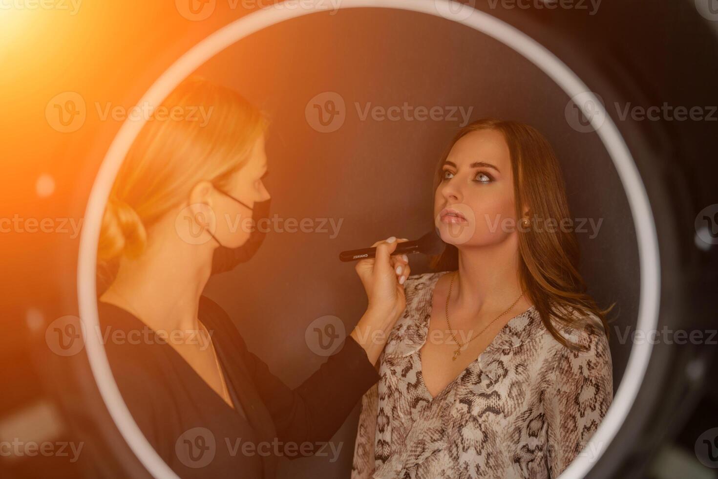 Makeup beauty salon. Makeup artist applies powder and blush. Beautiful female face. Makeup master's hand puts blush on cheeks of beauty model girl. Makeup in progress photo
