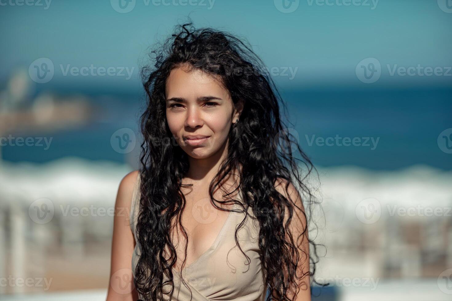 Sea woman rest. Portrait of a woman with long curly black hair in a beige dress stands on a balcony against the backdrop of the sea. Tourist trip to the sea. photo