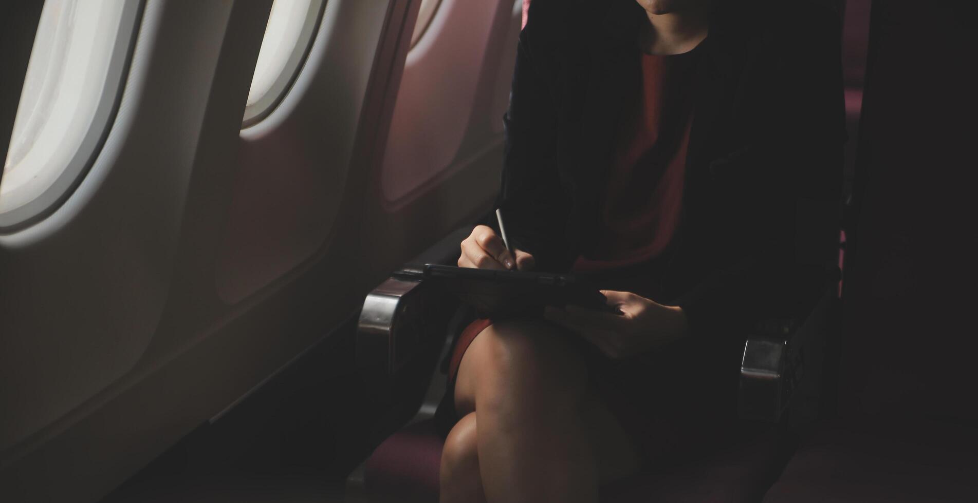 Blonde female tourist checking incoming notification on smartphone sitting on seat of airplane with netbook.Young businesswoman share media from telephone on laptop computer during plane flight photo