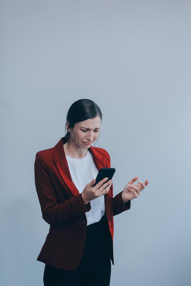 Annoyed angry young woman mad about spam message stuck phone looking at smartphone isolated on blank studio background, furious teen girl having problem with cellphone irritated by broken mobile photo