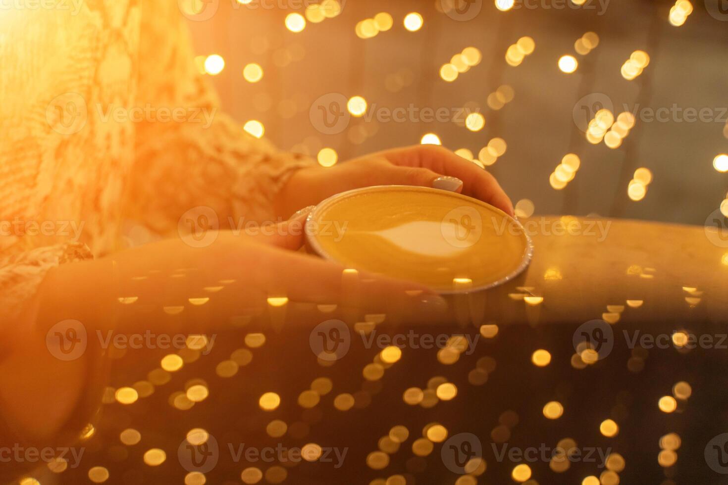 Close up Cup of coffee latte in coffee shop.Female hands holding a cup of coffee cup with heart shaped latte art foam on black wood table. photo