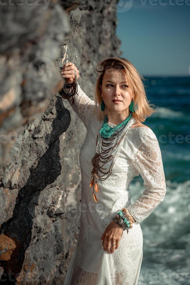 Middle aged woman looks good with blond hair, boho style in white long dress on the beach decorations on her neck and arms. photo
