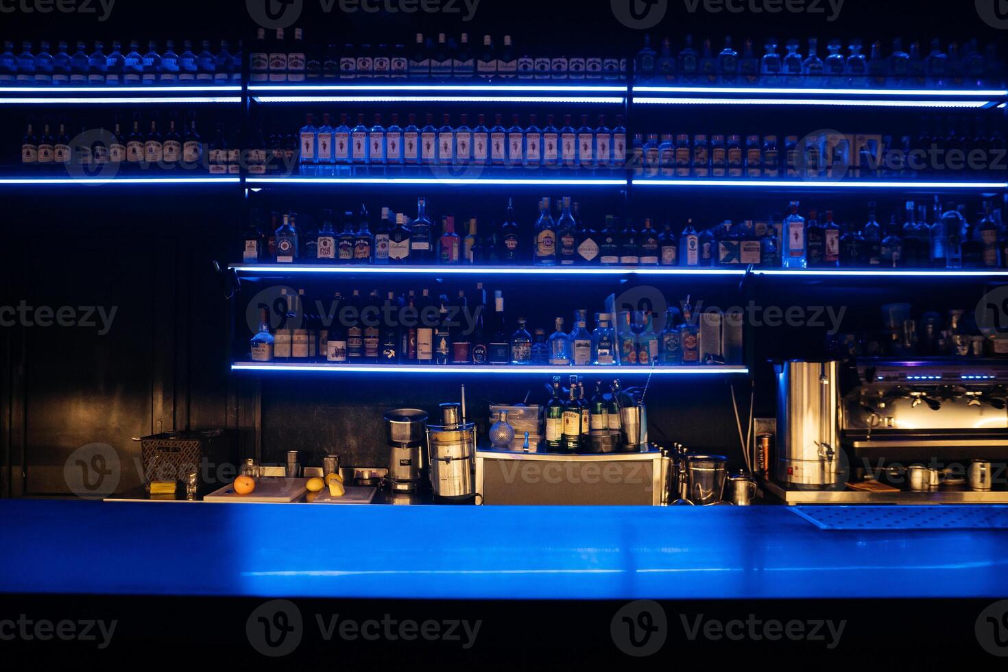 A bar with a blue counter and shelves of liquor. The bar is empty and the lights are on. photo