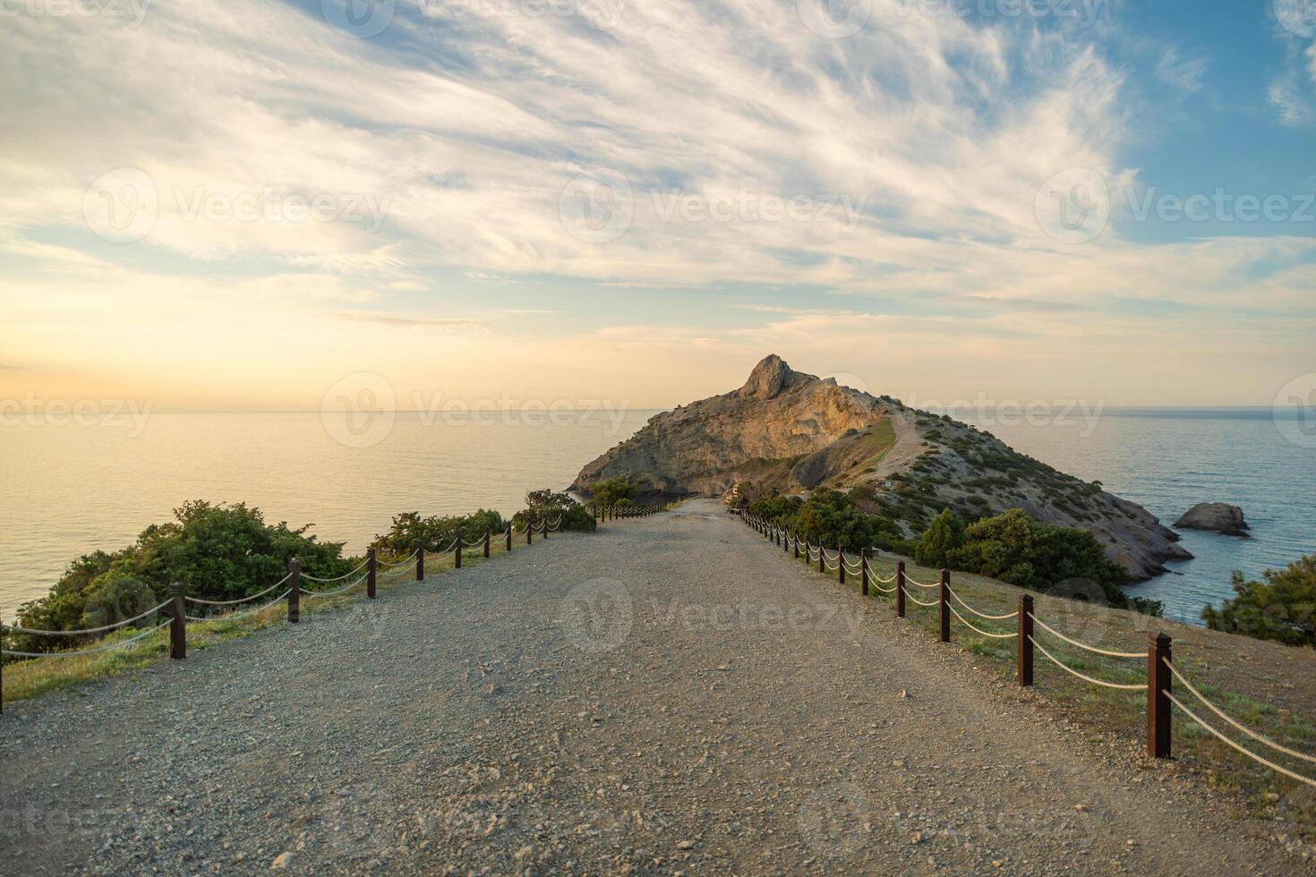A rocky beach with a long road leading to a cliff. The road is lined with wooden posts and the sky is cloudy. photo