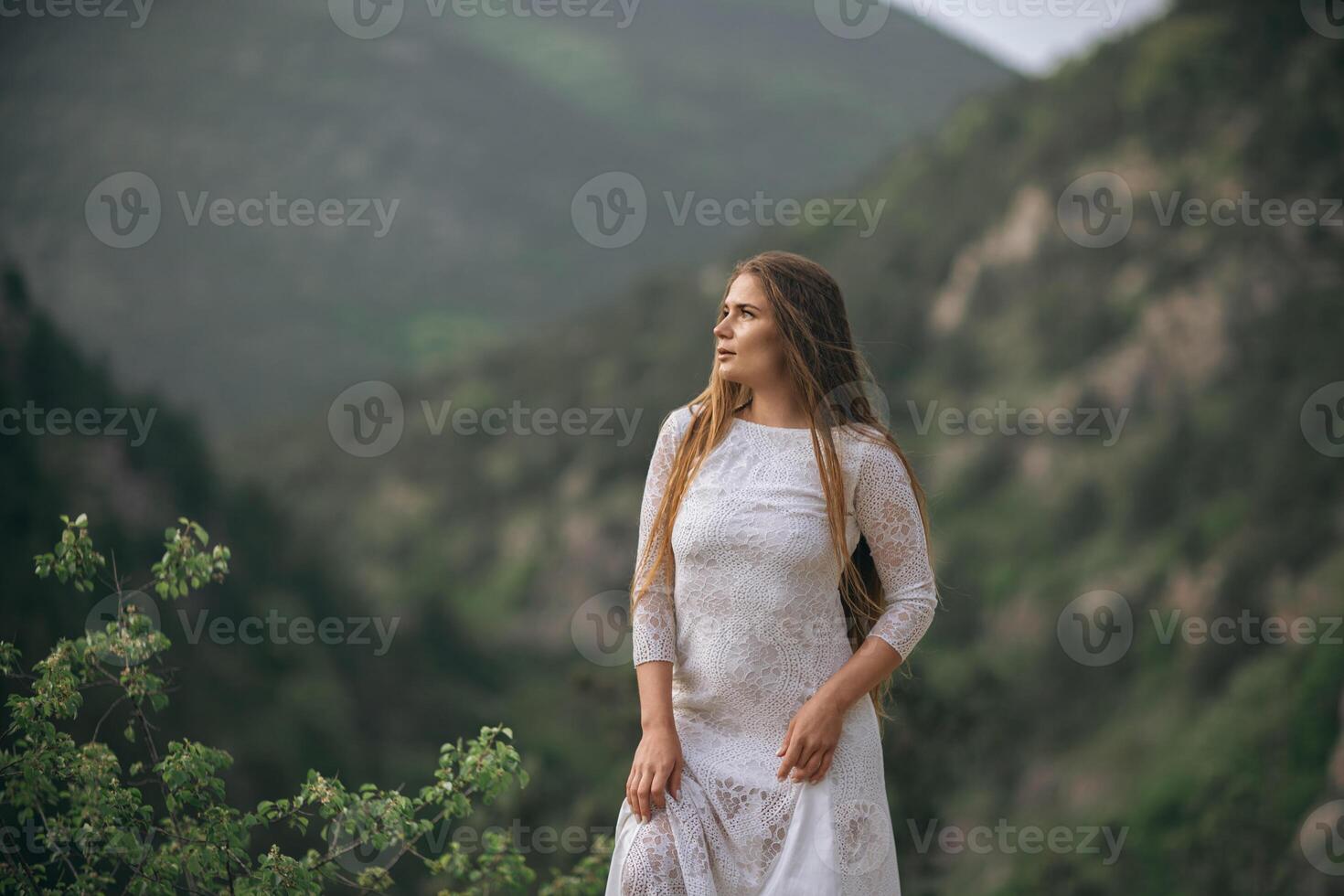 A woman in a white dress stands on a mountain top photo