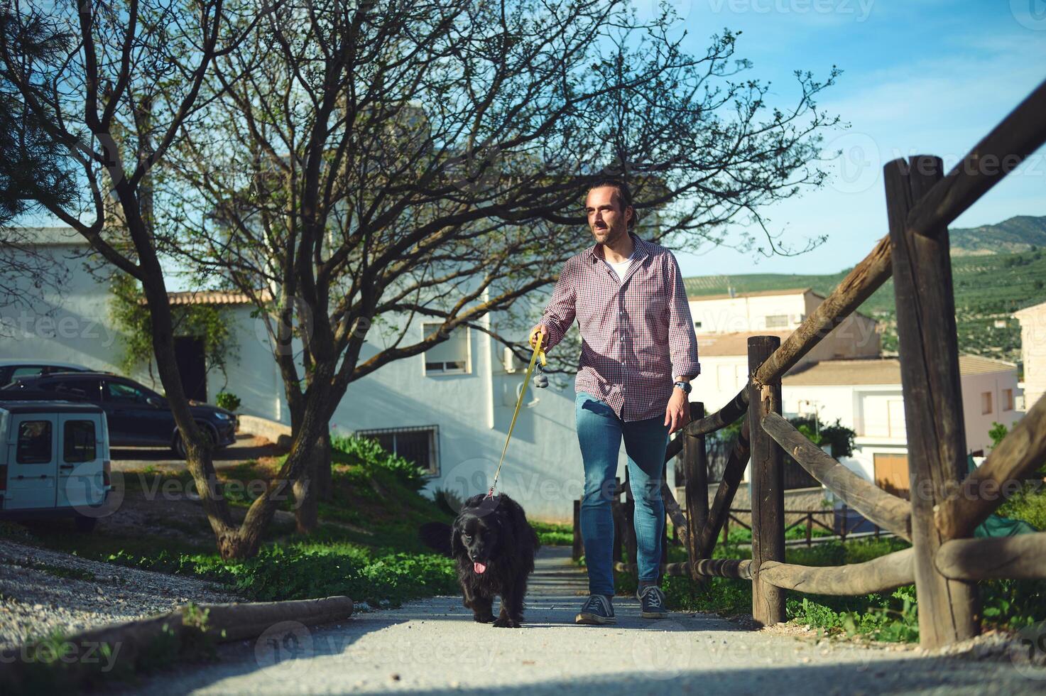 Smiling happy Caucasian man walking his dog, a black cocker spaniel on leash on the nature. People and animals photo