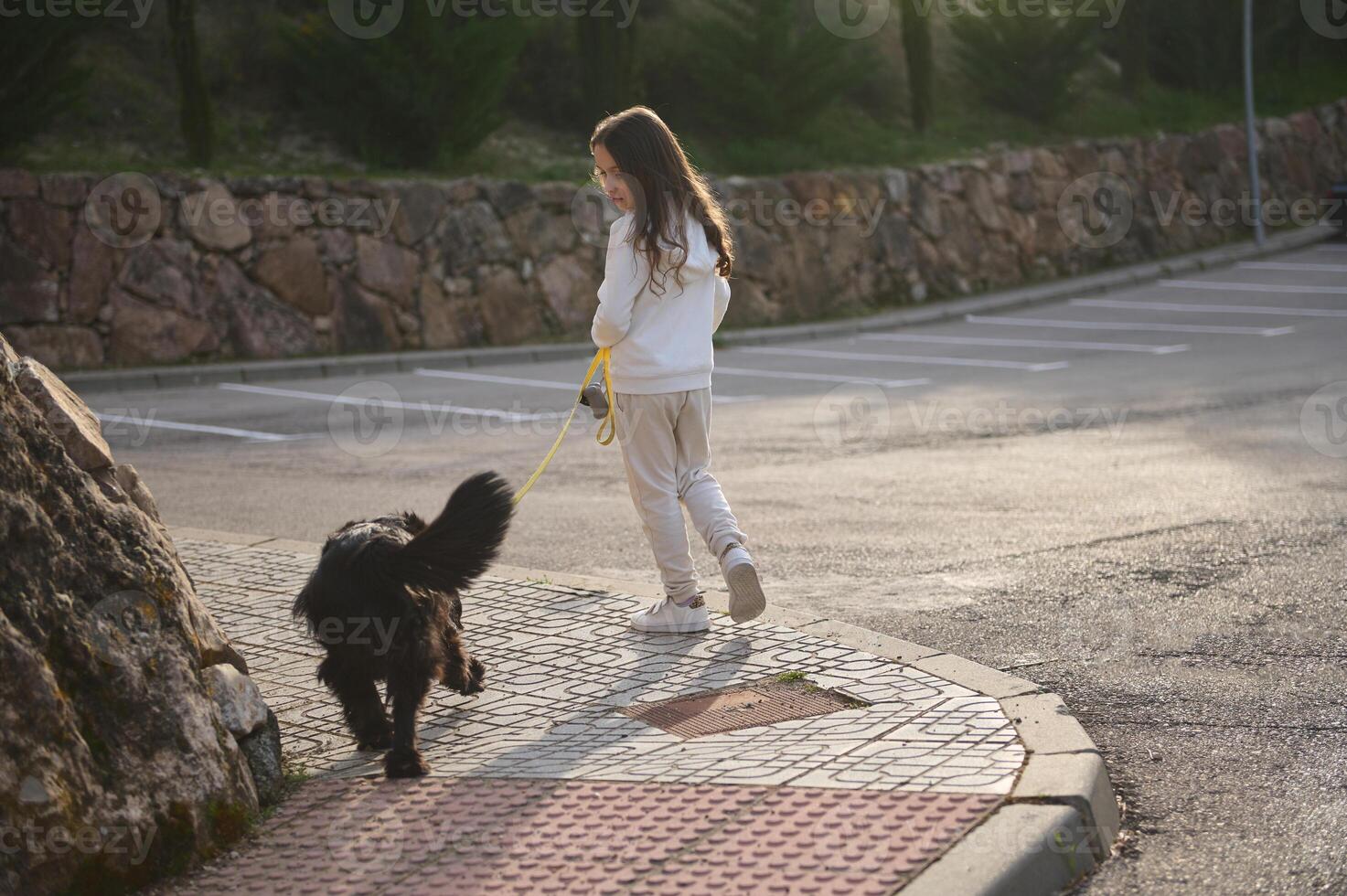 Full length portrait of a beautiful little child girl in sportswear, walking her dog on leash on the street outdoors. People and animals. Playing pets concept photo