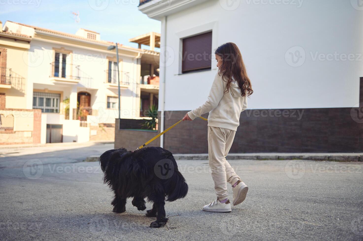 Happy adorable little child girl walking her dog on leash on the city street. Pets and children. Playing pets concept photo