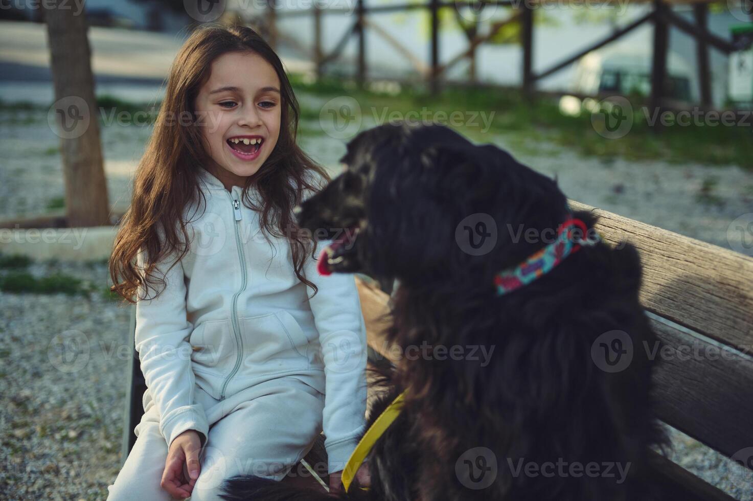 Cute smiling little kid girl playing with her favorite pedigree dog friend while walking outdoors in the city park. Cheerful elementary age child enjoying happy time with her pet in the nature photo