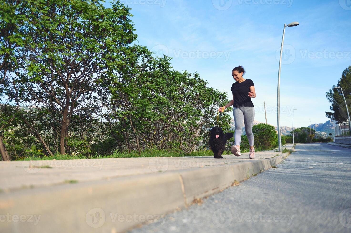 Front view of a young active woman walking her dog on leash in the nature on a beautiful sunny summer day. Pretty female athlete running with her pet in the morning photo