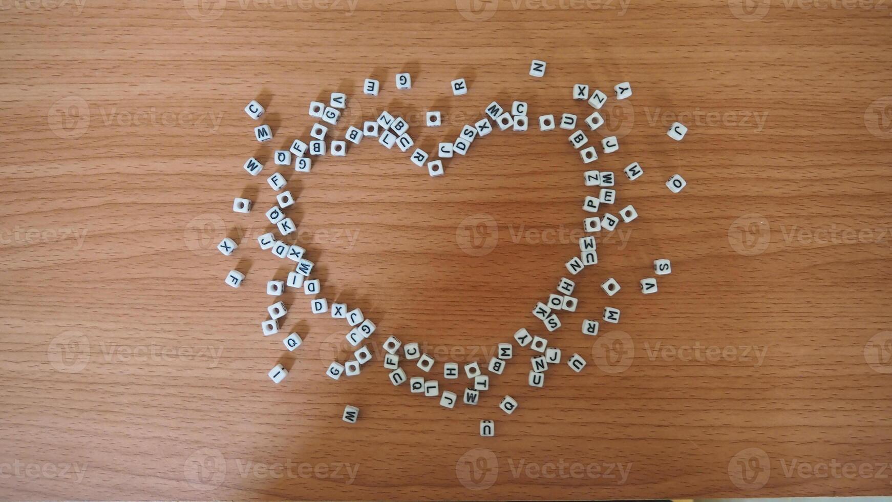 Heart from alphabet white beads blocks with letters in heart random letters around top view wooden background photo