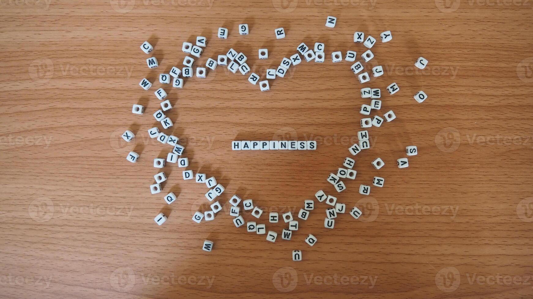Happiness - words from alphabet white beads blocks with letters in heart, random letters around, top view wooden background photo
