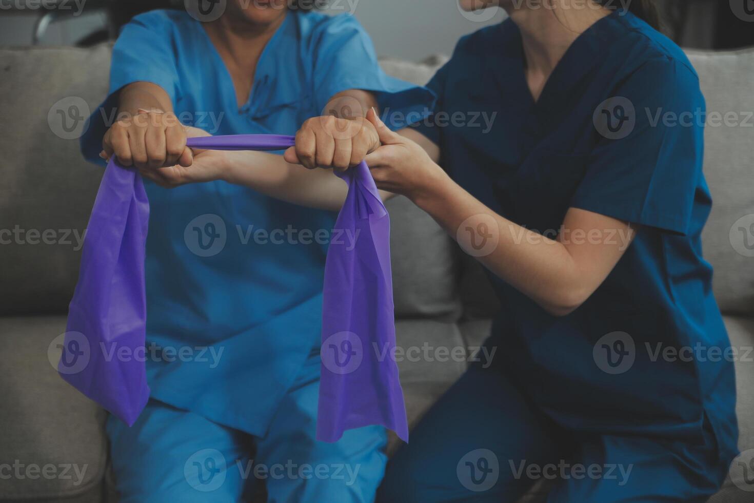 Personal trainer assisting senior woman with resistance band. Rehabilitation physiotherapy worker helping old patient at nursing home. Old woman with stretch band being coached by physiotherapist. photo