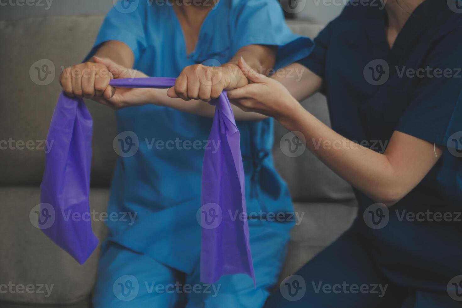 Personal trainer assisting senior woman with resistance band. Rehabilitation physiotherapy worker helping old patient at nursing home. Old woman with stretch band being coached by physiotherapist. photo