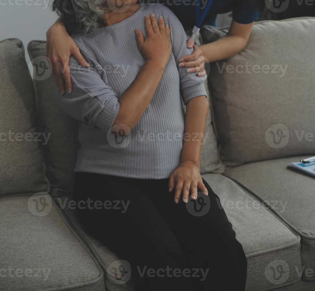 Smiling kind pleasant young female doctor in white uniform visiting disabled elderly mature patient at home, asking about health condition at checkup meeting, geriatric healthcare help concept. photo