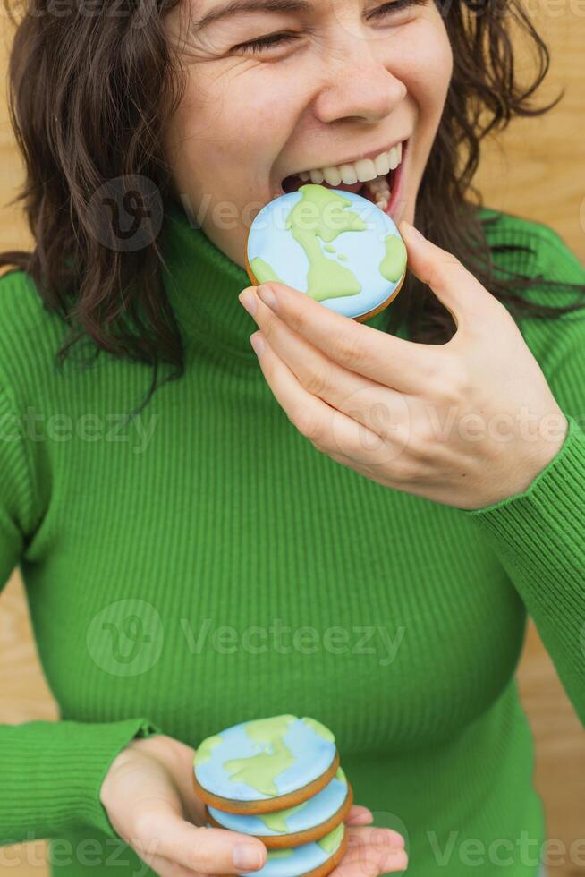 Earth Day concept. Woman bites into a cookie in the shape of the Earth. photo
