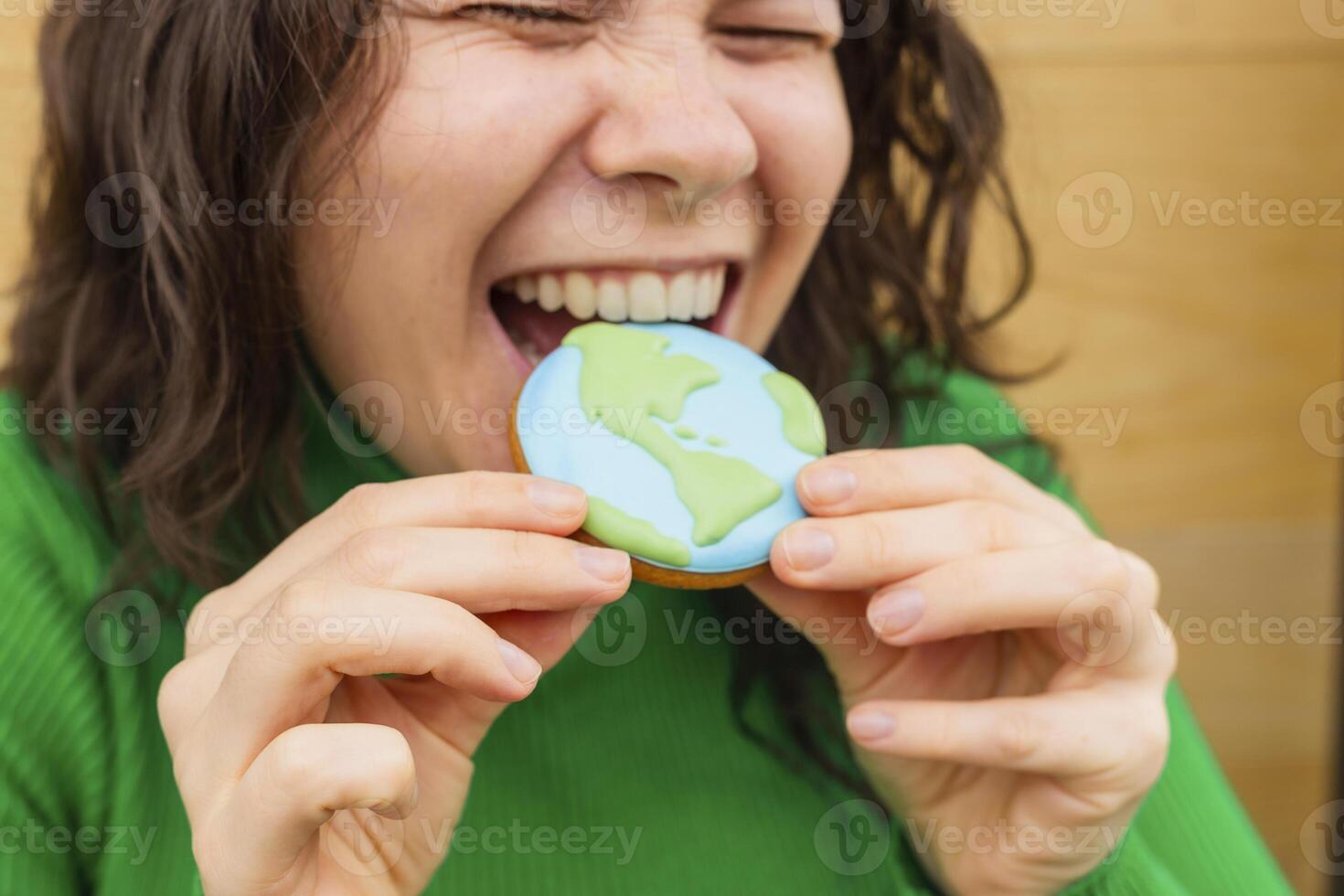 Earth Day concept. Woman bites into a cookie in the shape of the Earth. photo
