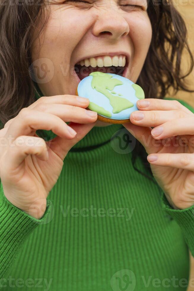 Earth Day concept. Woman bites into a cookie in the shape of the Earth. photo