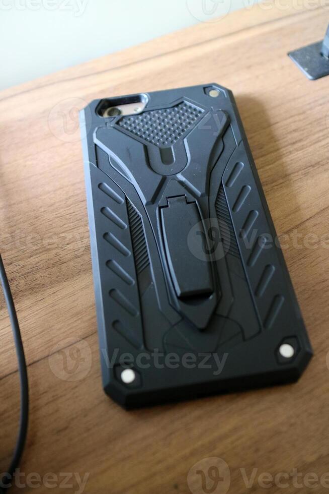 a smart phone with a black hard case with a robot style. placed on a wooden table photo