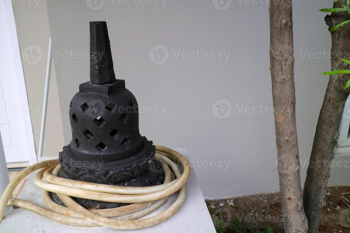 an artificial stupa made of cement. For outdoor decoration. black, with a water hose wrapped around it photo