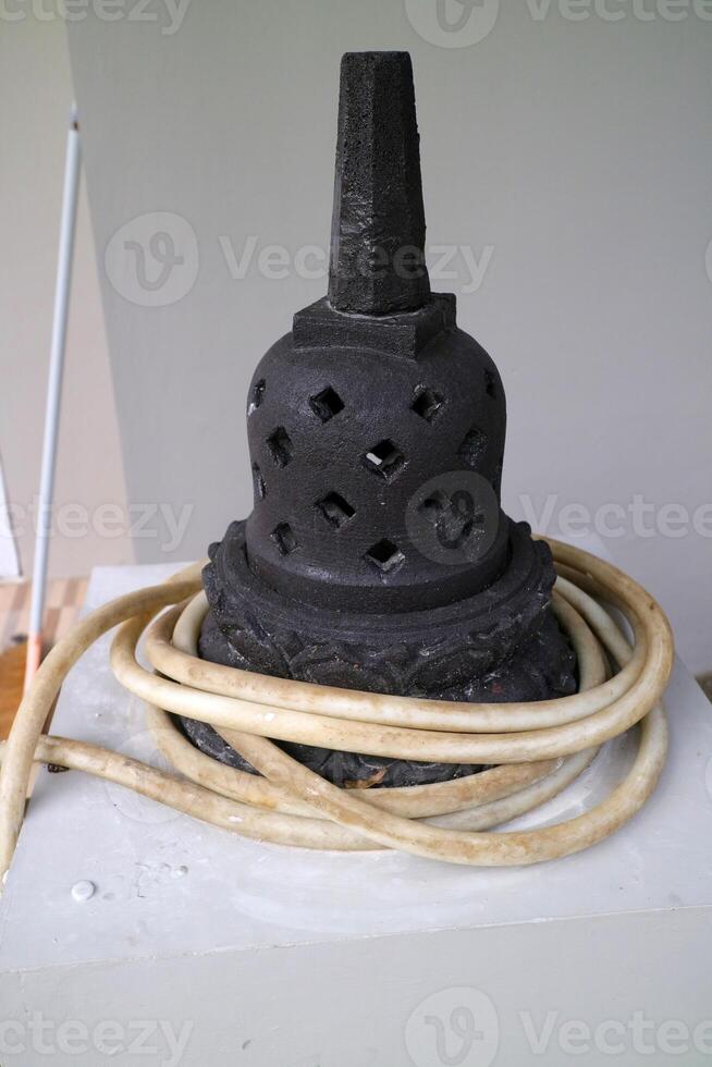 an artificial stupa made of cement. For outdoor decoration. black, with a water hose wrapped around it photo