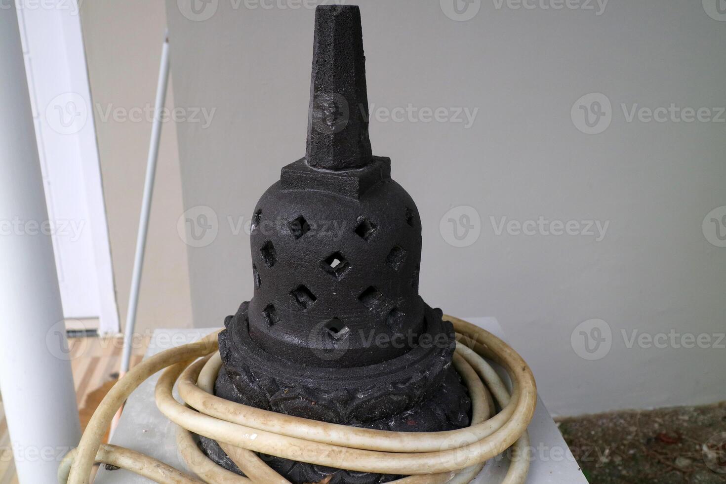 an artificial stupa made of cement. For outdoor decoration. black, with a water hose wrapped around it photo