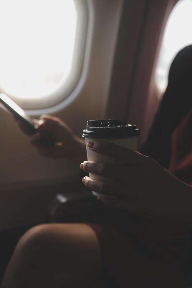 Blonde female tourist checking incoming notification on smartphone sitting on seat of airplane with netbook.Young businesswoman share media from telephone on laptop computer during plane flight photo