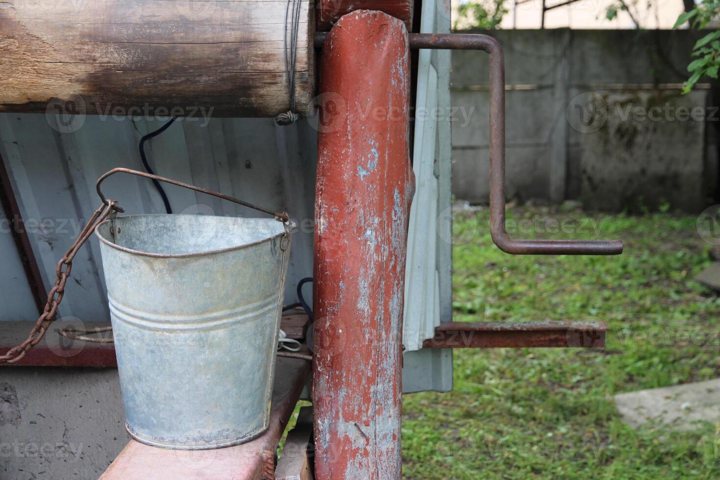 A close-up of an iron aluminum bucket standing near a rustic well on a farm. Device for extracting water in agriculture photo