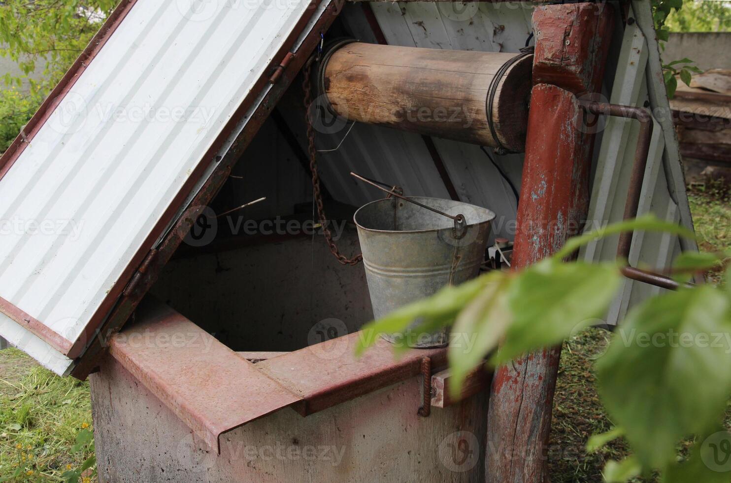 un antiguo bien para obtención agua con un bettón círculo, un hierro tapa, y un Iniciar sesión para levantamiento un Cubeta de agua. un dispositivo en pueblos para extrayendo agua desde subterráneo en agricultura en un granja foto