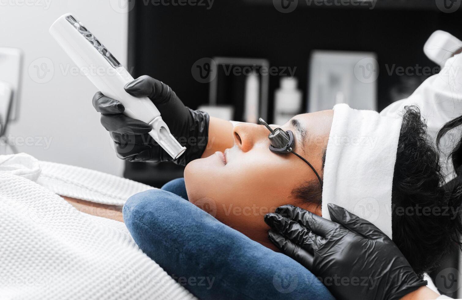Hands of a Professional Using a Laser For Skin Care on a Young Latin American Man. photo