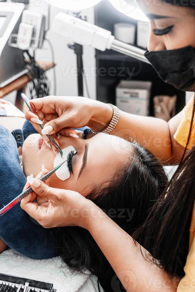 Hands holding tweezers while performing eyelash extension attachment. photo