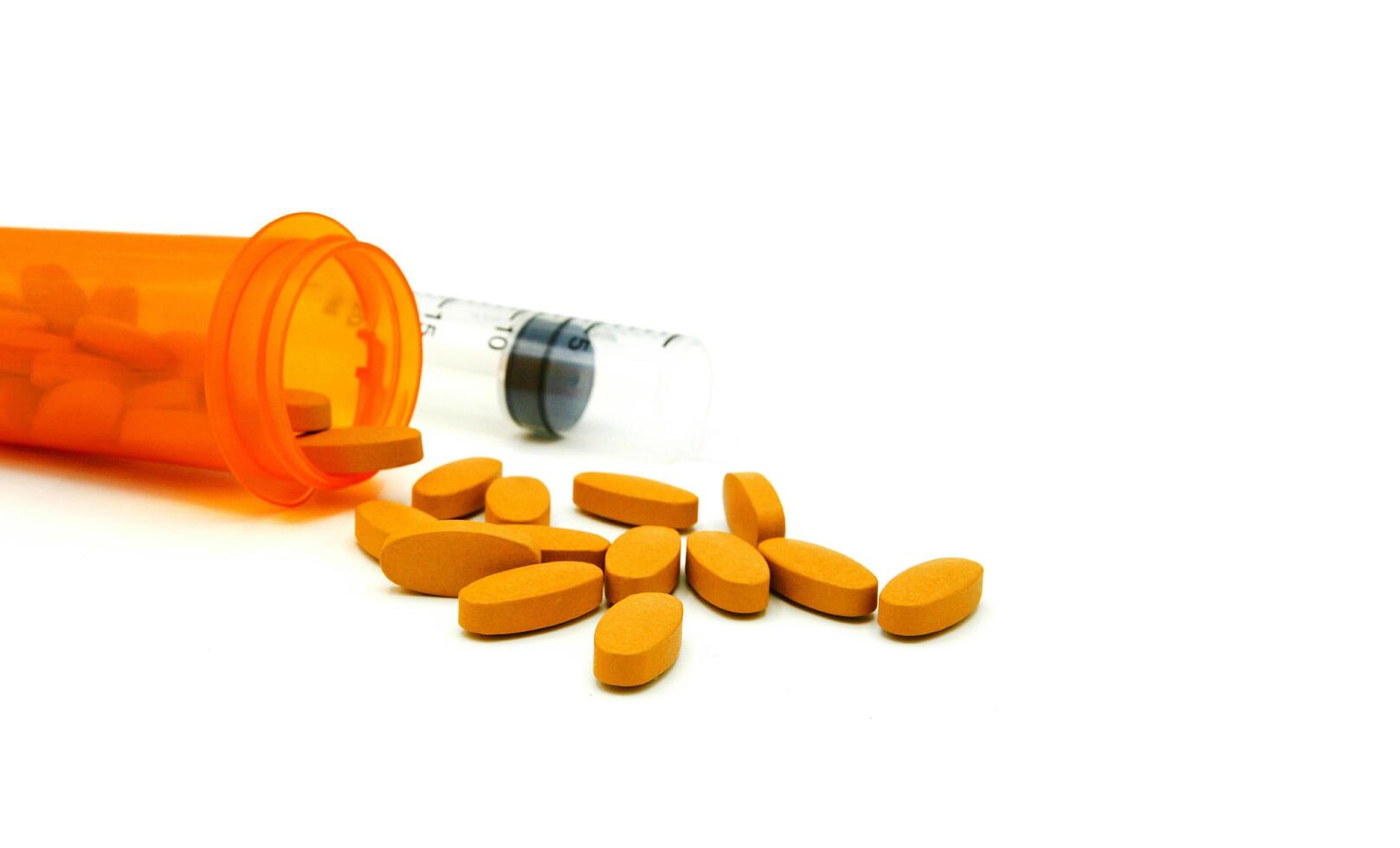 Many yellow pills out of the orange bottle of medicine and blurred plastic injection with copy space isolated on white background. Medical and Medicine with healthy concept photo