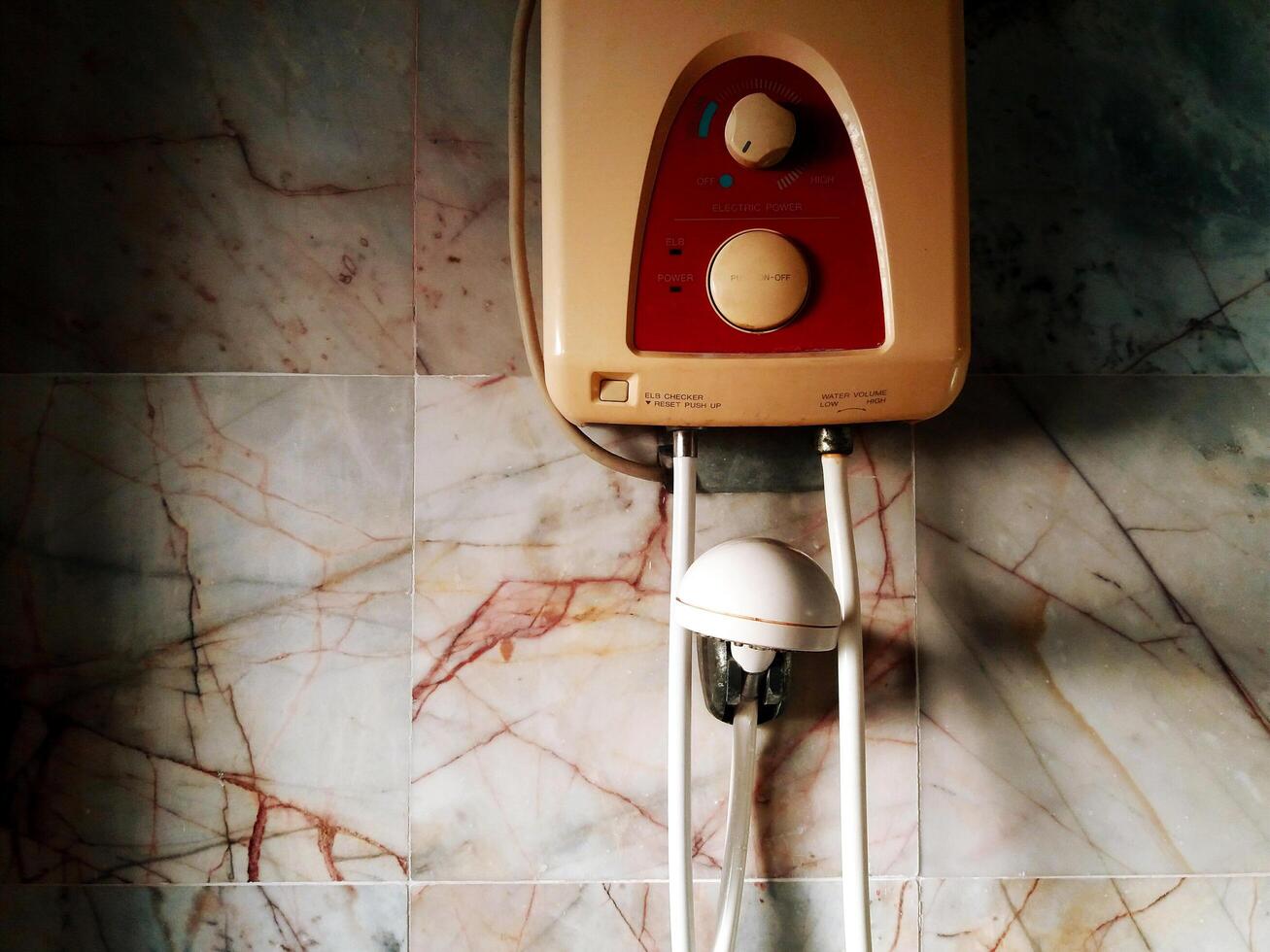 Old water heater installed on white, gray or gray marble wall inside restroom, washroom or toilet for making water warm and shower in winter. Electronic device with copy space. photo
