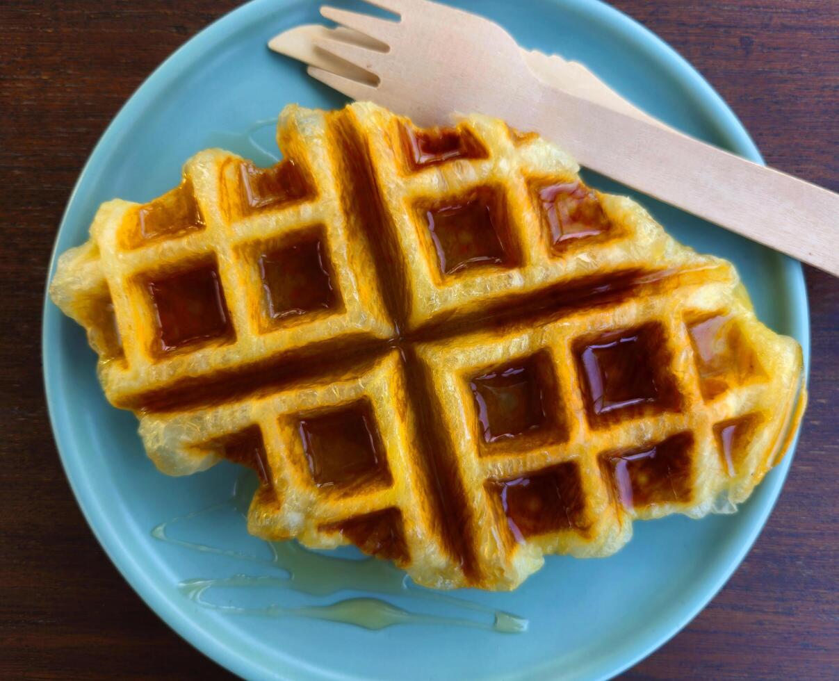 de cerca gofre coronado con miel salsa en azul plato a cafetería. dulce panadería en plato en de madera mesa o antecedentes con Copiar espacio. foto