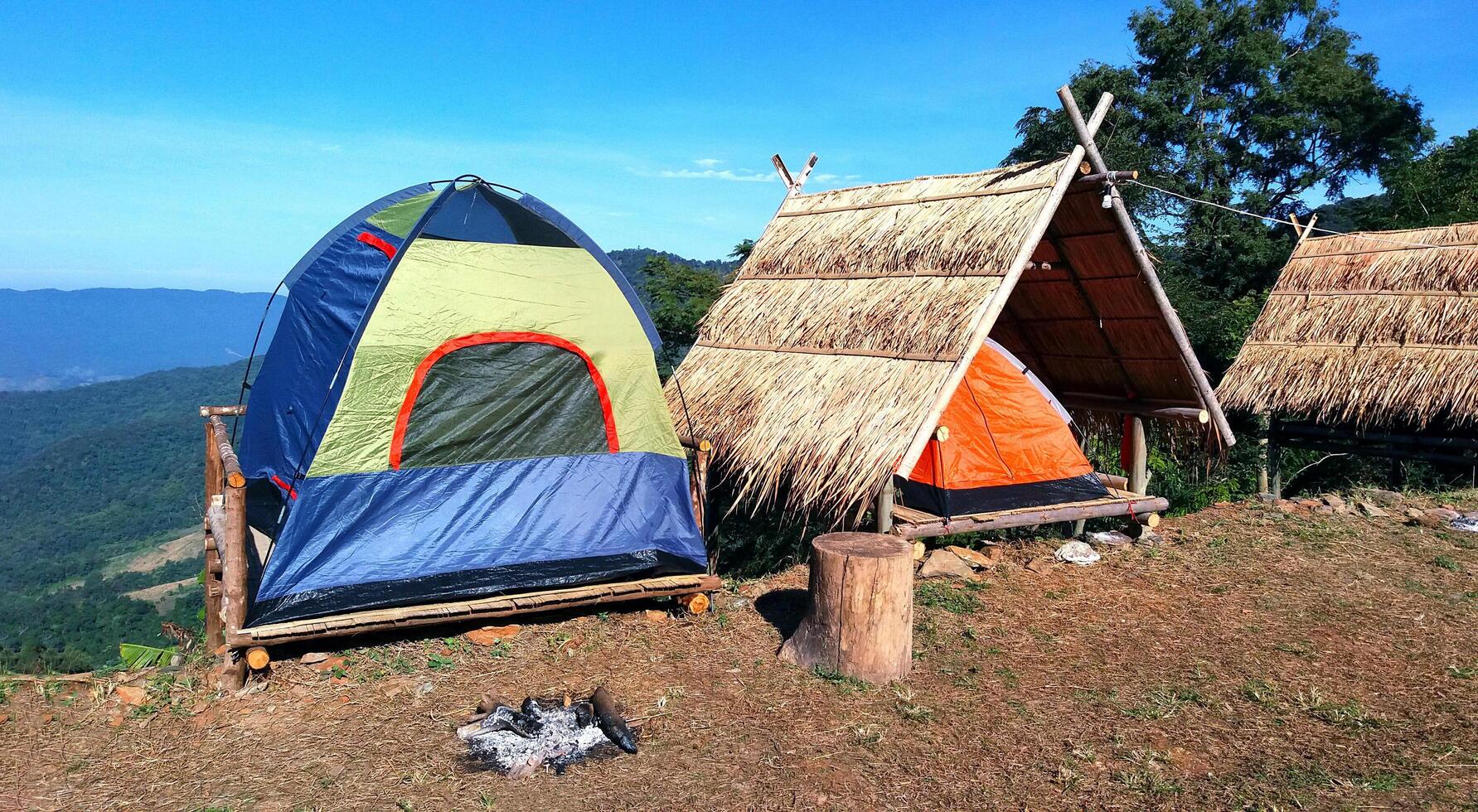 The camping blue, Green and orange tent on wooden litter with dry leaves roof and blue sky, mountain and tree foreground in summer time. photo