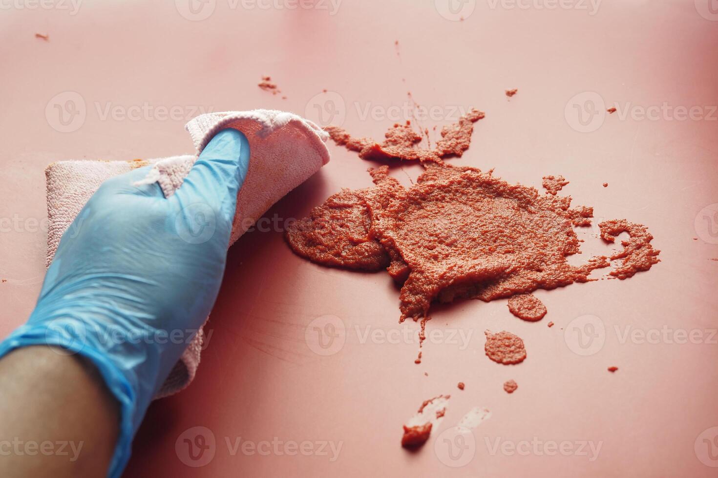 hand in blue rubber gloves cleaning tomato sauce spill with towel photo