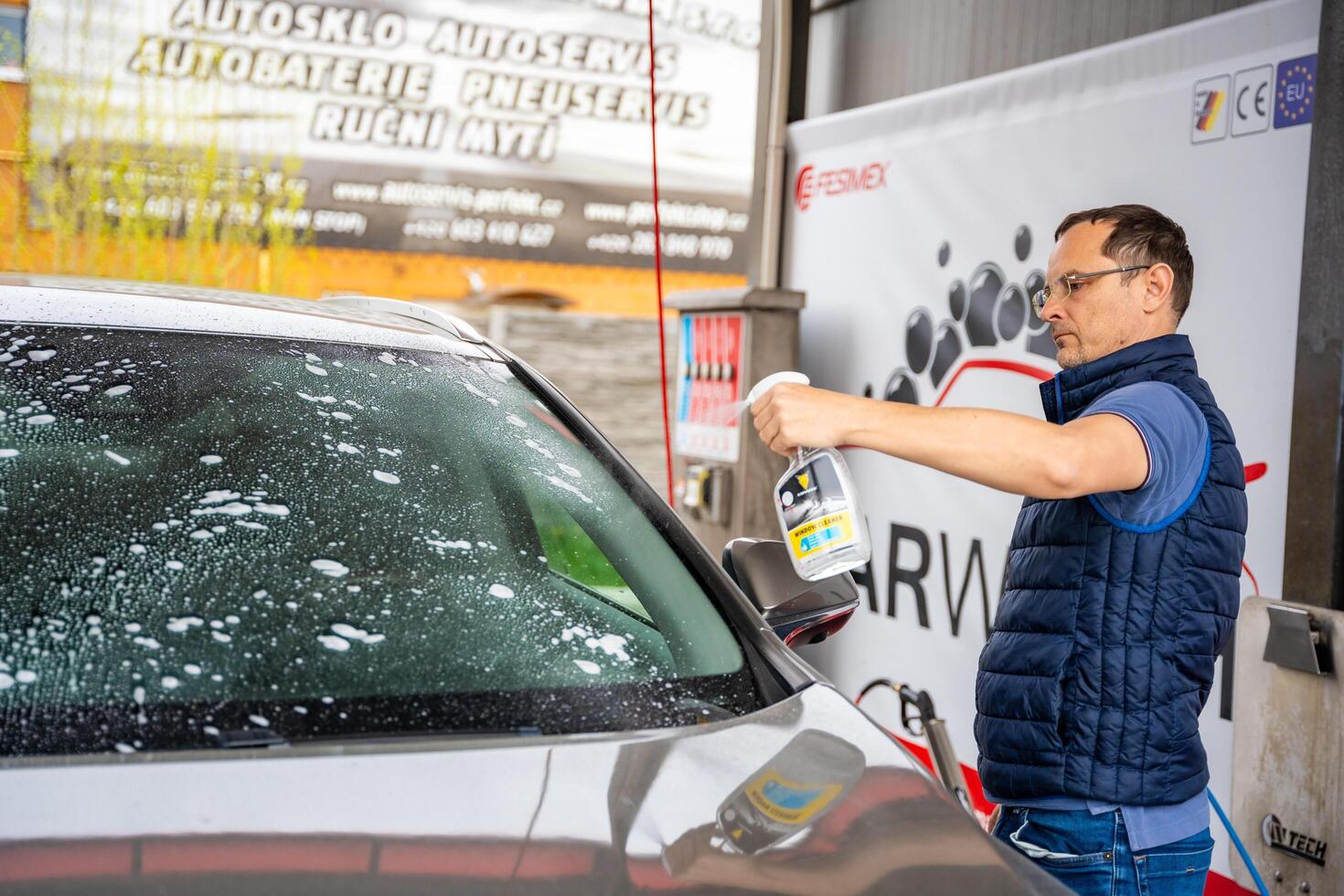Prague, Czech Republic - April 5, 2024. Young man applies liquid to clean windows of the car in self-service car wash. High quality photo