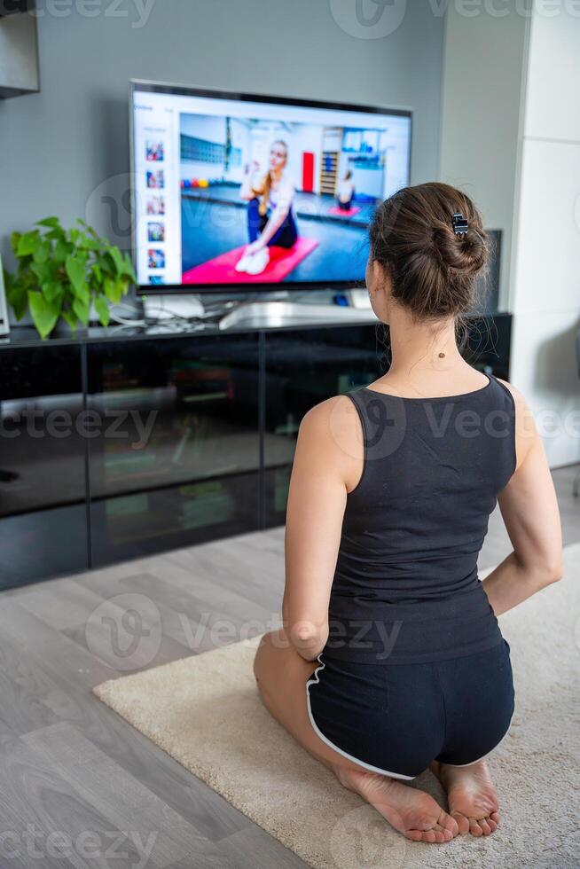 Young woman is doing fitness at home in living room while watching and participating in a class photo