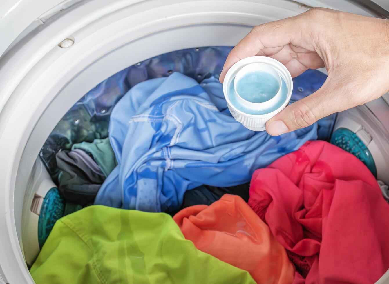 Hand holding laundry detergent with colorful clothes in washing machine photo