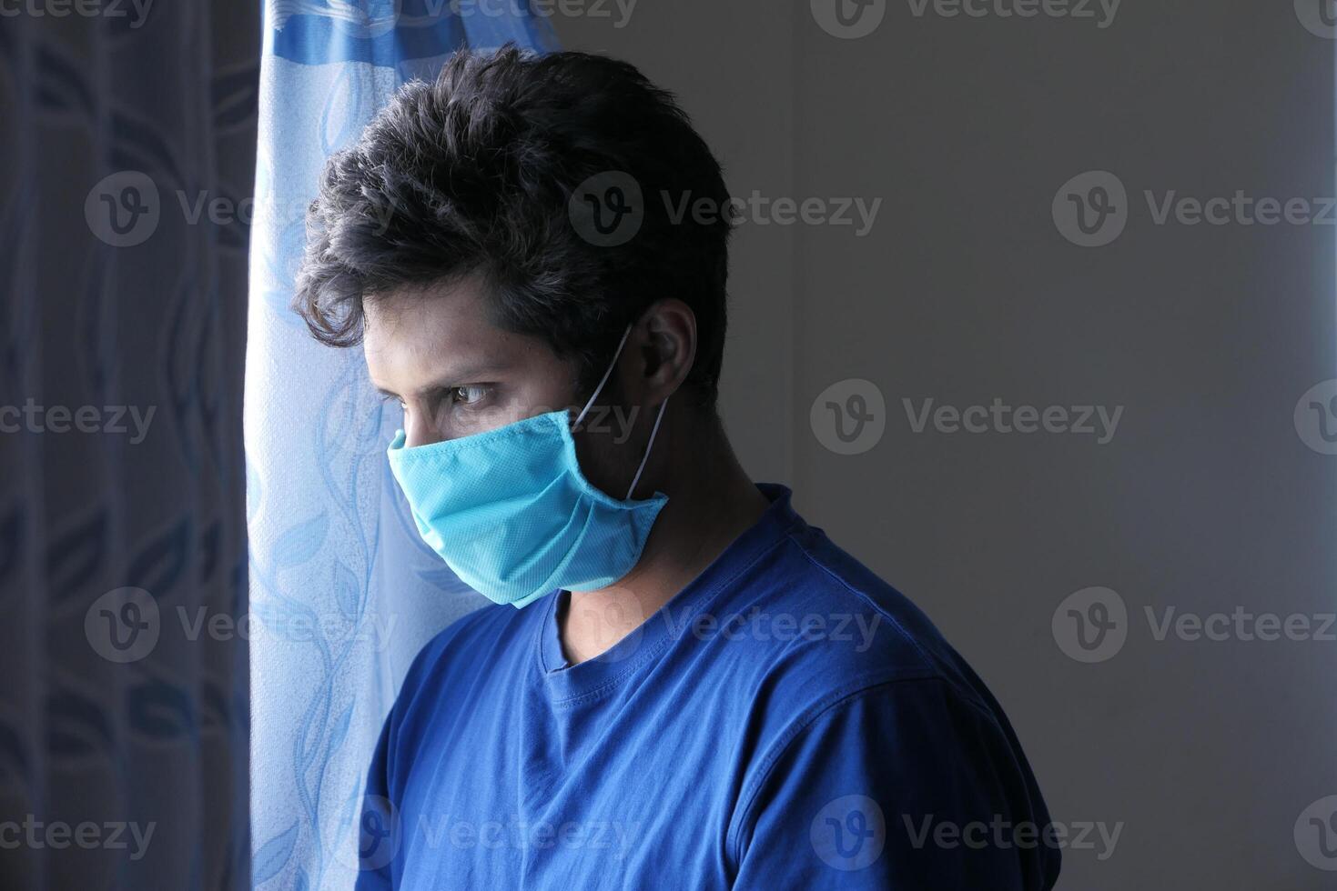 A sick man with a mask on his face looking through window photo
